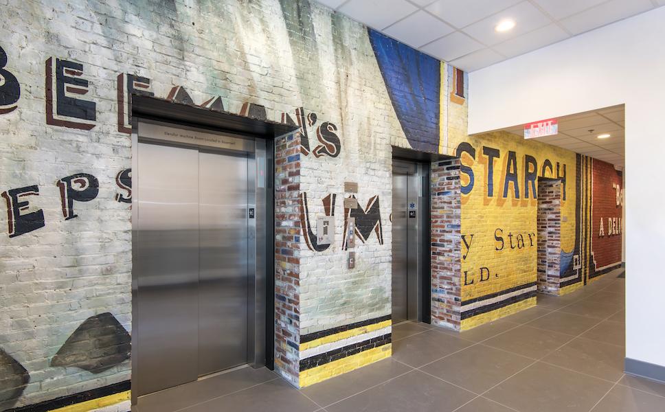 Elevator lobby; brick wall covered by mural with lettering and varied backgrounds.